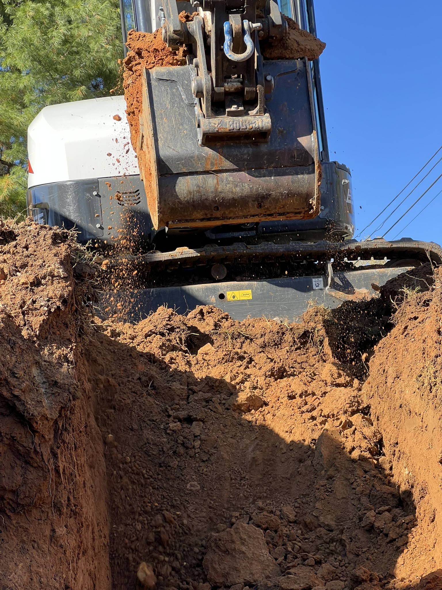 Excavator digging a utility trench through red clay soil